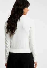 Vit tröja med texturerade prickar, långa ärmar och ribbat avslut. Slät tyg och figurnära design i en avslappnad stil.