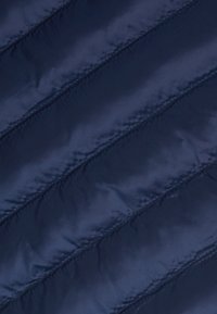 Marineblauwe geborduurde stof met diagonale stiknaden, een gladde textuur en een iets glanzende afwerking. Lichtgewicht en waterafstotend materiaal.