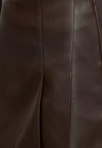 Tissu en cuir brun foncé avec des lignes de couture verticales et une couture centrale formant un pli subtil.