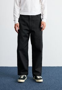 Pantaloni neri con una vestibilità dritta, dotati di passanti per cintura e tasche laterali, abbinati a una camicia bianca a maniche lunghe e sneakers nere.