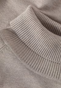 Tessuto lavorato a maglia beige chiaro con colletto a dolcevita a costine. La texture è liscia con diversi schemi di costine in tutto il tessuto.