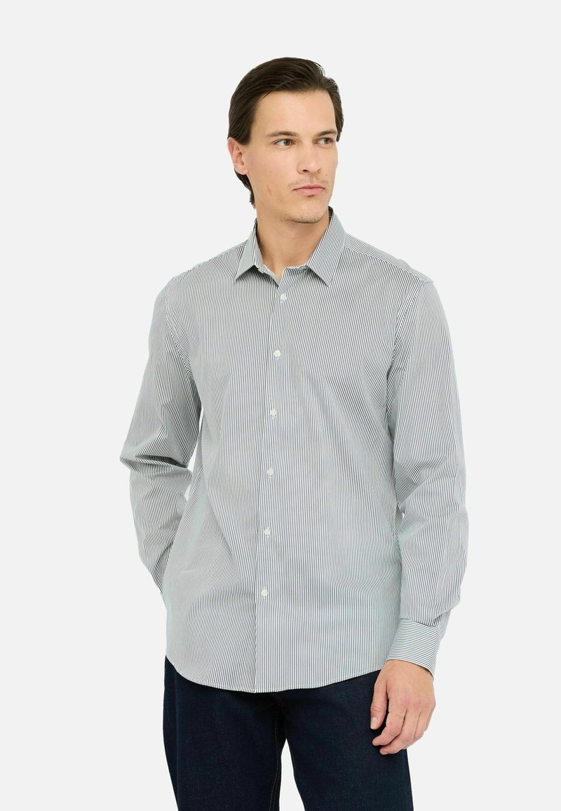 Gestreiftes langärmliges Hemd in Weiß und Marineblau mit Button-Down-Kragen, das über ein lässiges Design verfügt und über Knöpfe an der Vorderseite verfügt. Kombiniert mit dunklen Jeans.
