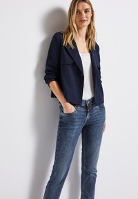 Chaqueta corta azul marino con dos bolsillos en el pecho, combinada con jeans de mezclilla azul claro. La tela parece suave y ligeramente estructurada.