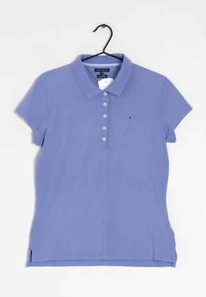 Jasnofioletowa koszulka polo z krótkim rękawem, zapinana na guziki, z małym logo po lewej stronie na piersi, zawieszona na czarnym wieszaku na białym tle.