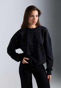 Sudadera negra con adornos de rhinestones, con cuello redondo y corte holgado. Tejido texturizado con puños y cinturilla acanalados.