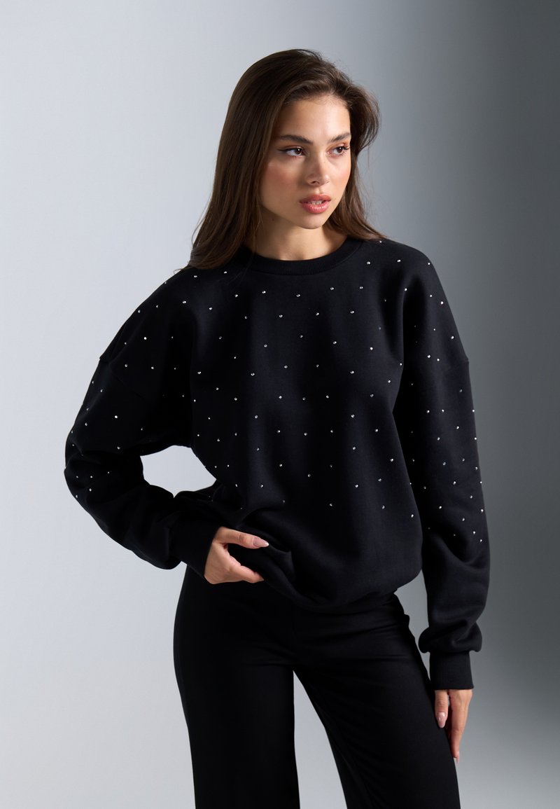 Sudadera negra con adornos de rhinestones, con cuello redondo y corte holgado. Tejido texturizado con puños y cinturilla acanalados.