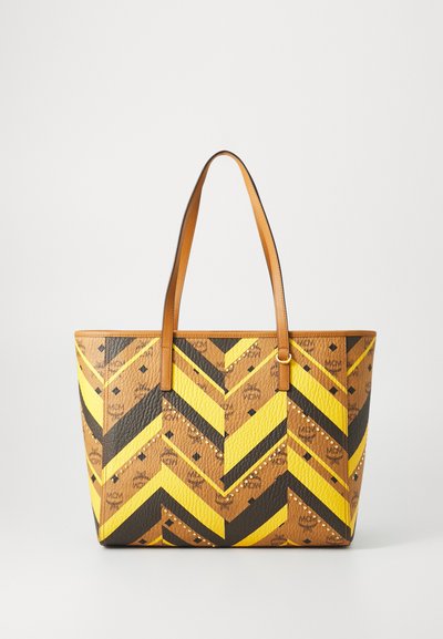 Tote bag with a chevron pattern in brown, yellow, and black. Textured material, leather handles, and studded accents add detail.