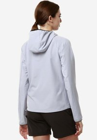 Giacca a vento grigia chiara con un sottile motivo a quadri, texture liscia e maniche lunghe, abbinata a pantaloni corti neri.