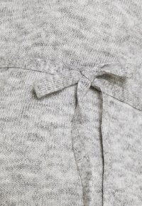 Tissu en tricot gris doux avec un gros plan sur un nœud noué réalisé à partir du même matériau, montrant les détails de la texture et des coutures.