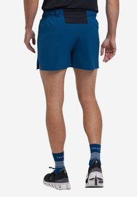 Pantaloni sportivi blu con una vita nera, caratterizzati da fessure laterali per la mobilità. Indossati con calze a righe blu e scarpe da corsa nere.