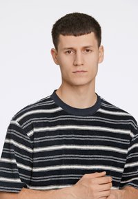 Camiseta de manga corta a rayas en blanco y negro con cuello redondo, que presenta un tejido texturizado y un corte relajado.