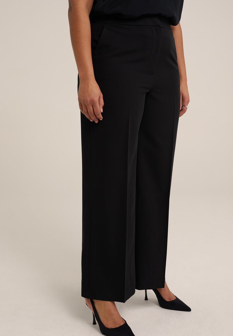 Pantalons larges noirs en tissu lisse, dotés de poches latérales et d'une coupe ajustée, associés à des talons noirs pointus.