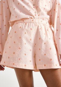 Ljust rosa shorts med persikomönster, tillverkade av ett lätt och texturerat material med elastiskt midjeband. Har små broderade persikodetaljer över hela plagget.