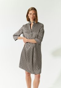 Mekko, jossa on musta ja kerma läiskäinen geometrinen kuvio, kauluksellinen pääntie, kolmannen neljänneksen hihat ja rento istuvuus.