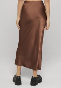 Jupe midi en satin marron à la texture lisse, avec une fente latérale, une taille haute, accompagnée de chaussures noires à semelles épaisses.