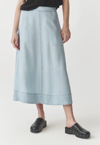 Svetlo modra denim midi krila s ravnim krojem in stransko žepoma; v kombinaciji s črnimi natikači s srebrnimi žebljički na podplatu.