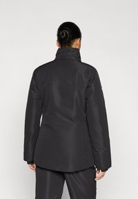 Μαύρο αδιάβροχο μπουφάν με ψηλό γιακά, μακριά μανίκια και ελαφρώς καμπυλωτό τελείωμα. Διαθέτει λεία υφή και κρυφές τσέπες με φερμουάρ.