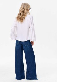 Witte blouse met wijd uitlopende mouwen, gecombineerd met wijde donkerblauwe spijkerbroeken. De outfit heeft een losse pasvorm en een soepele textuur.
