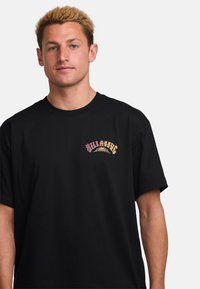Black cotton t-shirt featuring colorful graphic text on the left chest. The design includes circular elements and bold lettering.