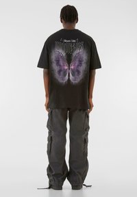 Black oversized t-shirt featuring a large butterfly graphic with purple accents on the back. Paired with dark cargo pants.