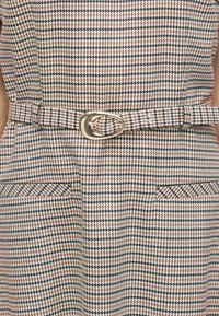 Καρό φόρεμα σε λευκό, μαύρο και σκουριά, με εφαρμοστή μέση και αγκράφα ζώνης σε χρυσό τόνο και δύο πλαϊνές τσέπες. Υφή υφάσματος.