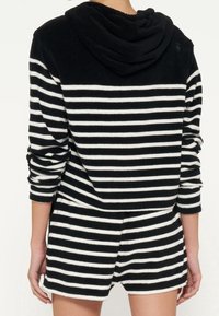 Tuta con cappuccio a righe bianco e nero, con una texture morbida, maniche lunghe e vestibilità rilassata. Presenta righe orizzontali e una fascia in vita.