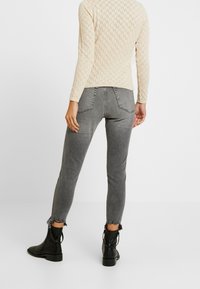 Dopasowane szare dżinsy z postrzępionymi końcami, wysoki stan i dwie tylne kieszenie, zestawione z teksturowanym kremowym swetrem z długim rękawem oraz czarnymi botkami za kostkę.