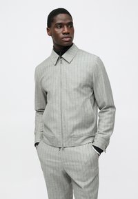 Siva jakna z navpičnimi črtami, ovratnikom, zadrgo in stranskimi žepi. Tkanina z reliefom ima navpične tanke črte, kombinirana z ujemajočimi hlačami.