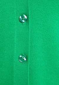 Cardigan verde lavorato a maglia con una texture liscia e due bottoni rotondi e lucidi sul davanti, ognuno con quattro fori per il fissaggio.