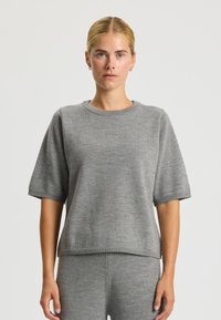 Maglione grigio chiaro a maniche corte con scollatura a girocollo e orli a coste. Realizzato in un morbido materiale a maglia, presenta una vestibilità comoda.