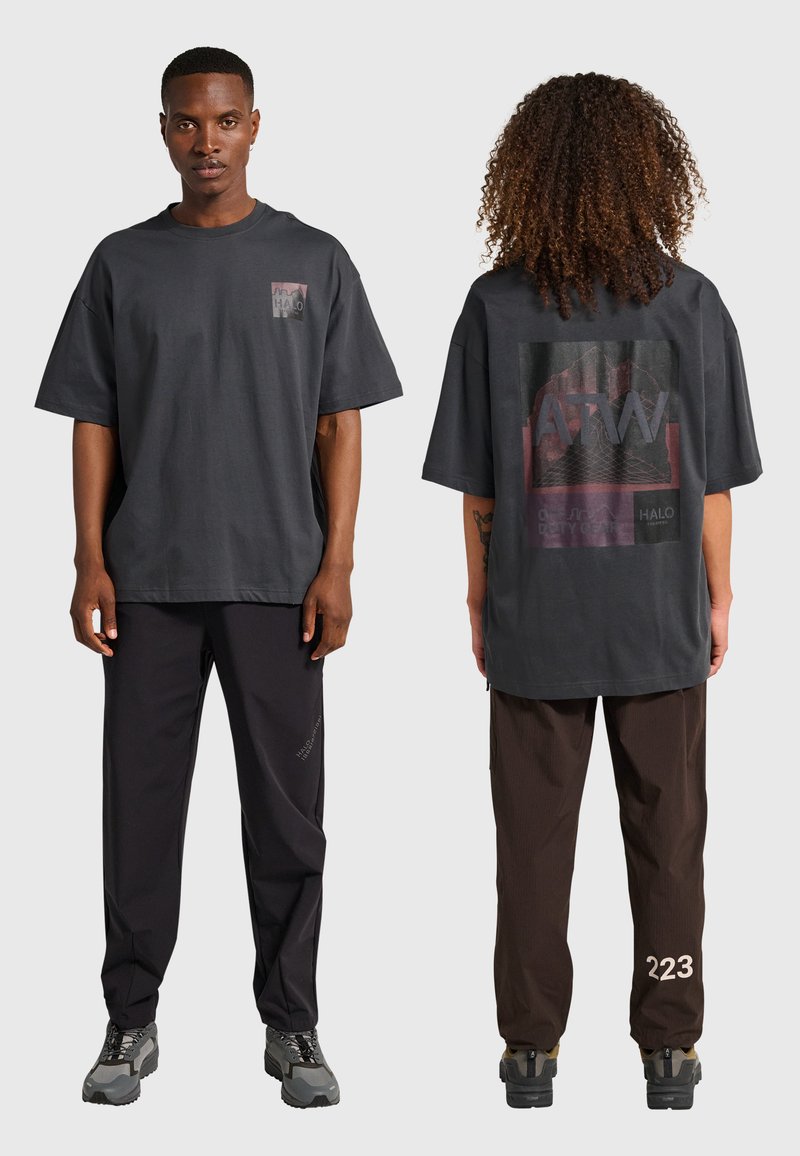 Dwa modele w oversize'owych, ciemnoszarych koszulkach z grafiką i casualowych spodniach, jeden zwrócony przodem, drugi pokazujący tylny wzór.