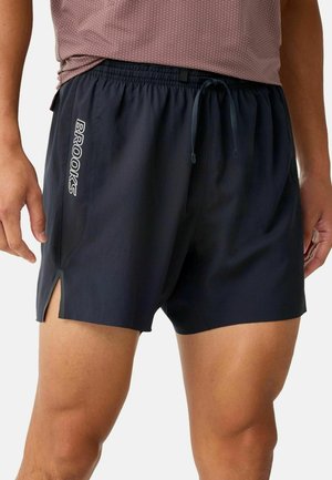 Mann trägt schwarze Sportshorts mit "Brooks" Logo auf der linken Seite und Kordelzug in der Taille, kombiniert mit einem dunkelroten Shirt.