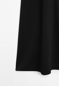 Sort stofgardin hængende mod hvid baggrund med bløde folder og glat tekstur.