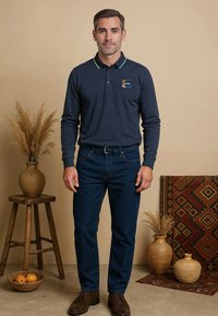 Marineblauwe polo met lange mouwen, een contrasterende kraag en een logo op de borst, gecombineerd met donkere jeans en bruine schoenen. Minimalistisch ontwerp met eenvoudige lijnen.