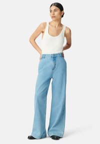 Jeans ampi in denim azzurro chiaro con vita alta e chiusura a bottone, abbinati a una canotta bianca. Texture liscia del denim con una vestibilità rilassata.