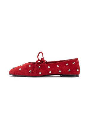 Zapato plano de ante rojo con tachuelas plateadas, un lazo en la parte superior y una pequeña suela negra mostrado de perfil.