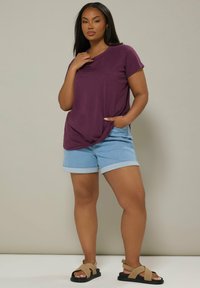 Lilla kortærmet t-shirt med en sidelomme, parret med lyseblå denimshorts med opkrøllede kanter og brune snøre sandaler.