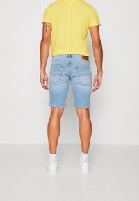 Světle modré džíny kraťasy se slim fit, roztrhaným lemem a designem s pěti kapsami. V kombinaci s žlutým tričkem s krátkým rukávem a bílými teniskami.