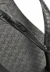 Chanclas de goma negras con una suela texturizada con patrones geométricos, tiras delgadas y grabado de la marca en la tira.