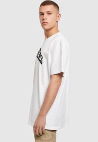Hvid bomulds T-shirt med korte ærmer, med sort trykt tekst på forsiden. Løs pasform, rund halsudskæring og glat tekstur.