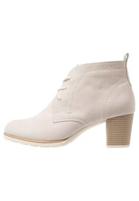 Stivaletto in camoscio beige chiaro con punta tondeggiante, chiusura con lacci e tacco impilato con dettagli testurizzati. Le cuciture aggiungono forma.