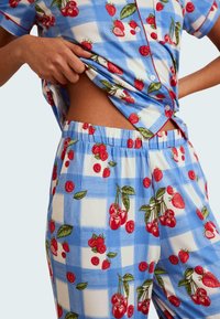 Blue checkered pajama set featuring red cherries and strawberries, short-sleeve button-up top and elastic-waist bottoms with vibrant fruit print.