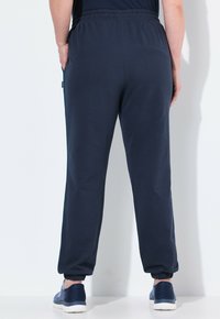 Navy blue sweatpants with an elastic waistband, side pockets, and tapered legs ending in elastic cuffs. Features a smooth, soft texture.