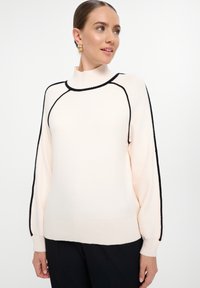 Suéter de punto rosa claro con un cuello alto, acentos negros a lo largo de las costuras y puños acanalados. Textura suave, corte relajado y mangas largas.