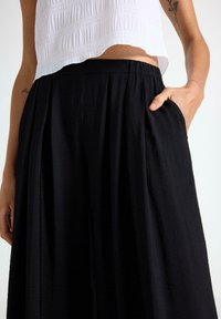 Sort plisseret nederdel lavet af letvægtsstof med elastisk talje og sidelommer, parret med en struktureret hvid cropped top.