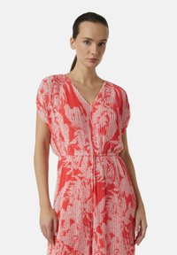Rot-weißer, gemusterter Kleid mit V-Ausschnitt und breiten kurzen Ärmeln, das eine geraffte Taille und plissierte Textur aufweist.