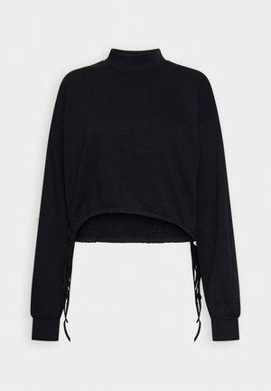 Sort cropped langærmet top med høj hals og justerbare sidestropper, vist fladt mod en hvid baggrund.