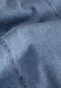 Tissu en denim, teinte bleu moyen avec une texture fine, caractérisé par des lignes verticales subtiles. Apparence douce et légèrement usée.