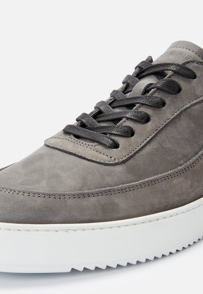 Szürke velúr sneaker, texturált felülettel, kerek orral és fekete fűzővel. Fehér gumitalppal rendelkezik, amelynek szélein fogazott minta található.