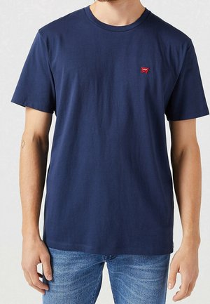 Navyblaue Baumwoll-T-Shirt mit kurzen Ärmeln, Rundhalsausschnitt und kleinem roten Logopatch auf der Brust. Glatte Textur, lässige Passform.